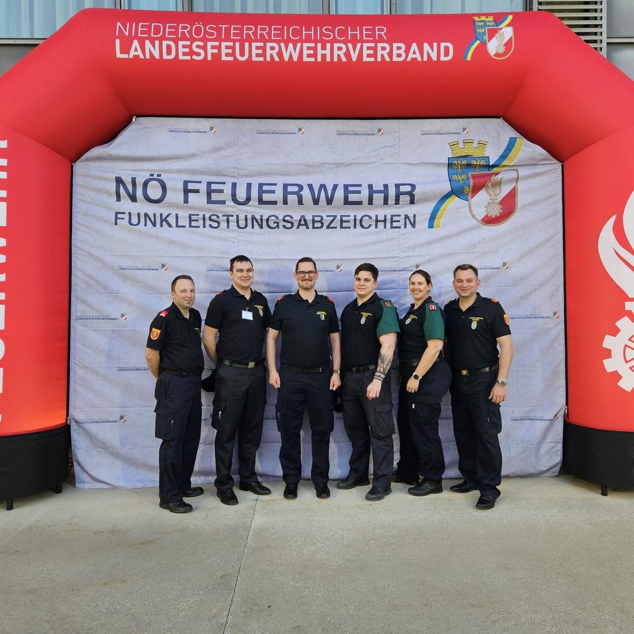 Sechs Feuerwehrleute in Uniform stehen vor einem Banner mit der Aufschrift 'Keine Feuerwehrsignale'. Dahinter befindet sich ein roter Bogen mit der Aufschrift 'Niederösterreichischer Feuerwehrverband'.