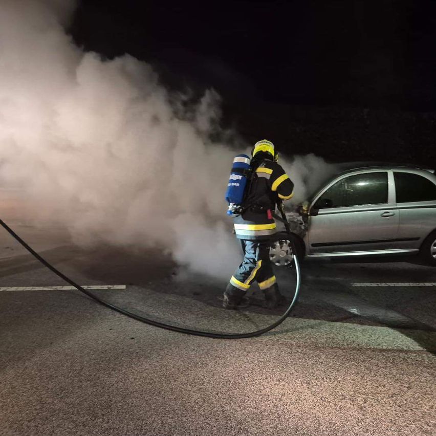 Ein Feuerwehrmann sprüht mit einem Schlauch Wasser auf ein rauchendes Auto bei Nacht.