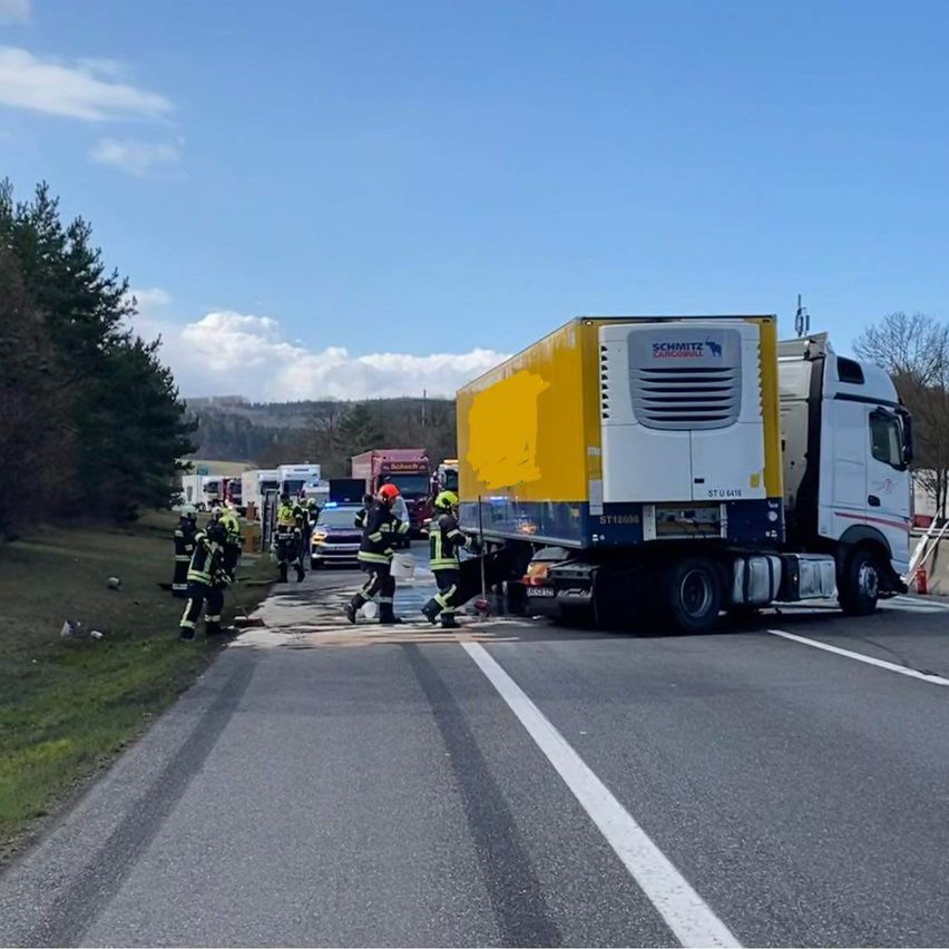 Ein Lkw-Unfall hat auf der Straße stattgefunden, wobei Feuerwehrleute am Unfallort arbeiten. Mehrere Rettungsfahrzeuge sind geparkt.