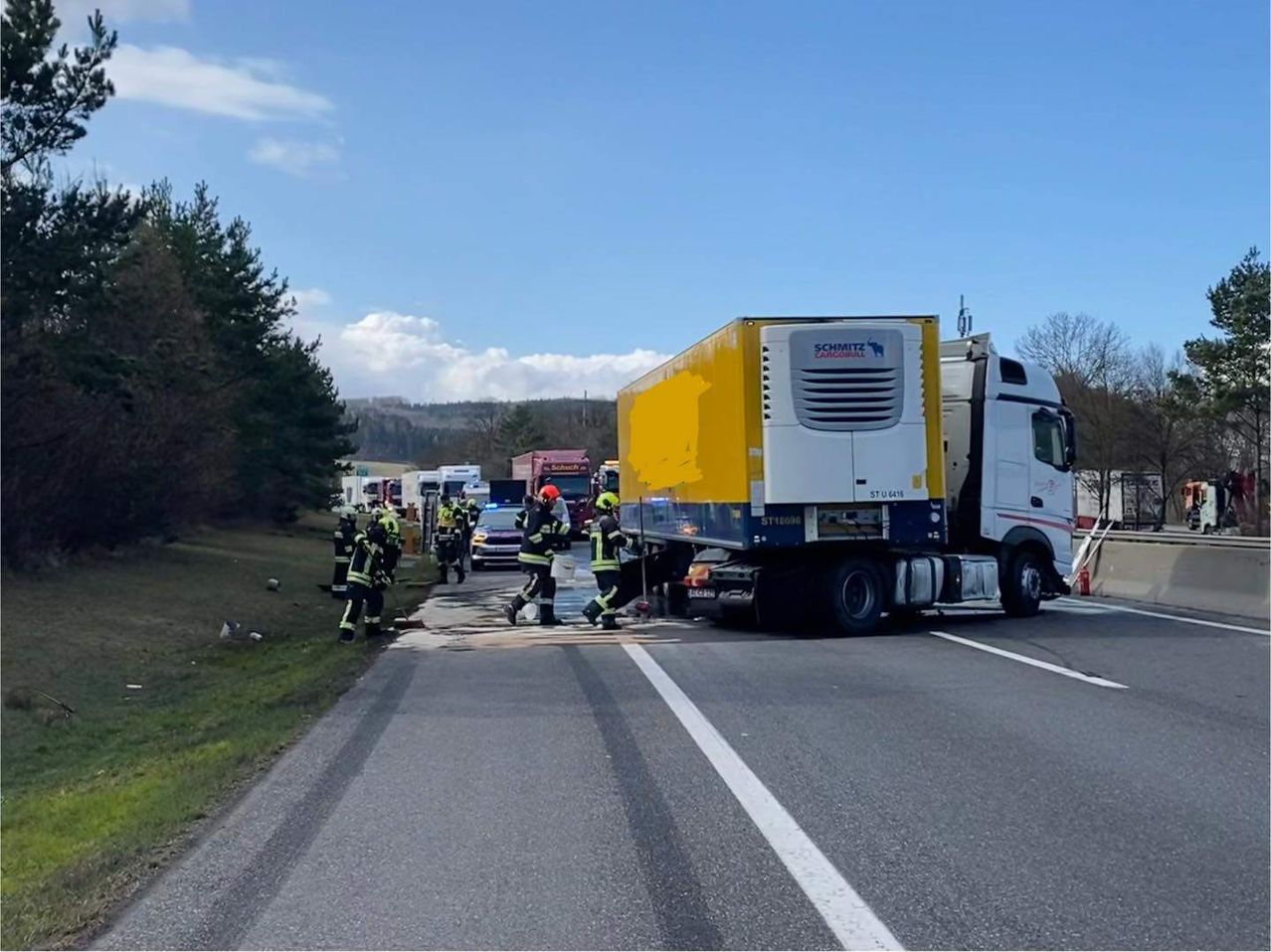 Ein Lkw-Unfall hat auf der Straße stattgefunden, wobei Feuerwehrleute am Unfallort arbeiten. Mehrere Rettungsfahrzeuge sind geparkt.
