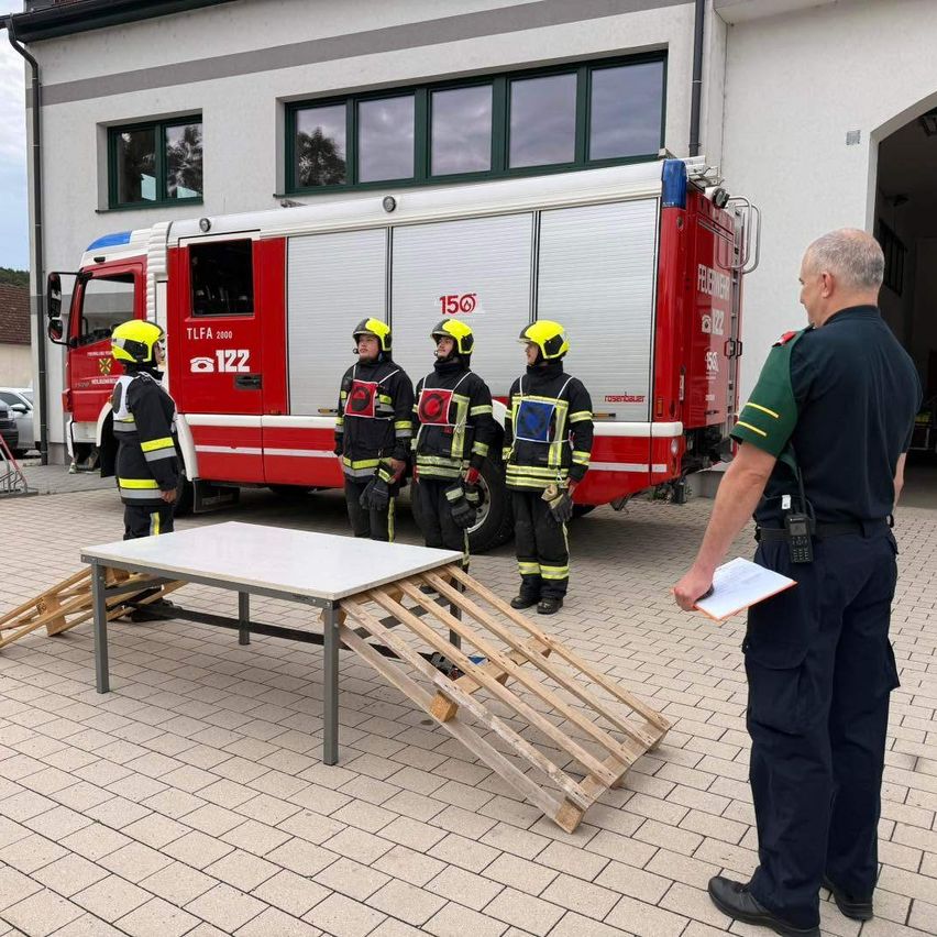Vier Feuerwehrleute in gelben Helmen stehen vor einem Feuerwehrauto mit einem Mann, der einen Klemmbrett hält.