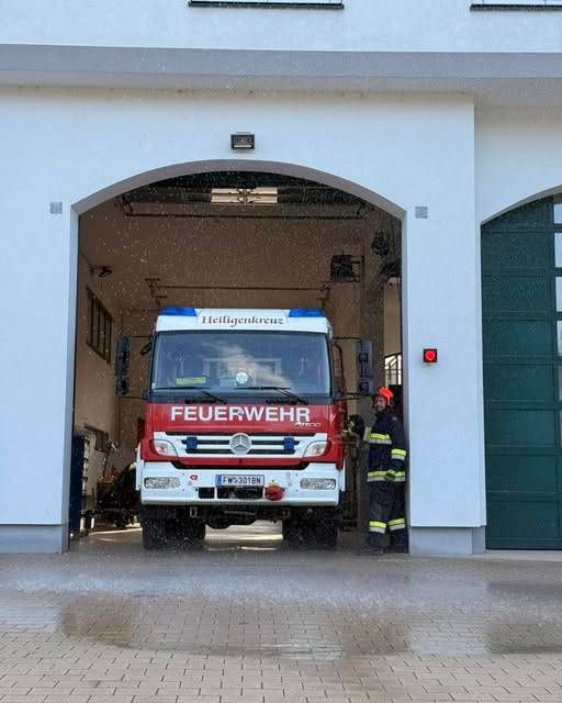 Ein Feuerwehrauto steht in einer Feuerwache, ein Feuerwehrmann steht daneben.