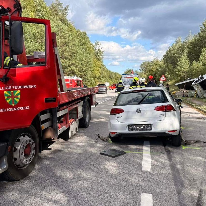 Rettungskräfte an der Unfallstelle eines Autos mit einem roten Abschleppwagen und einem weißen Auto am Straßenrand.