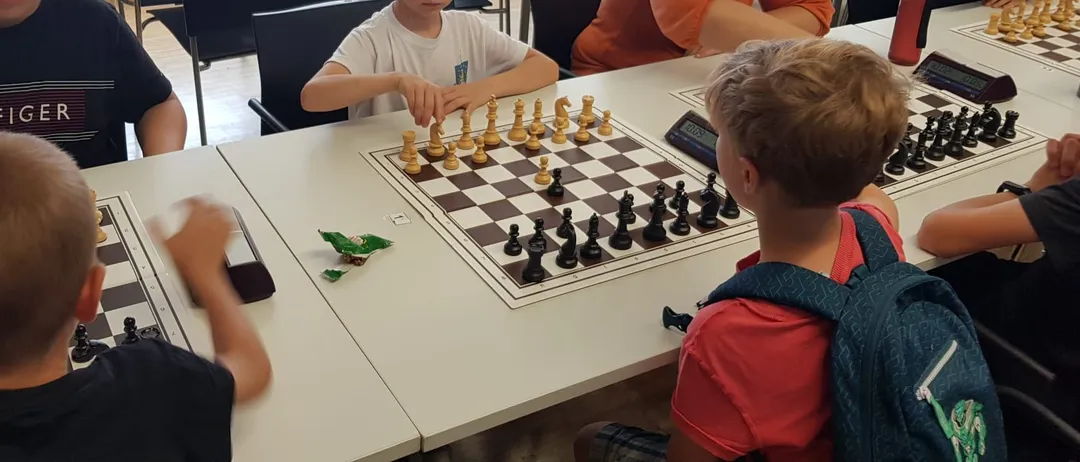 Eine Gruppe von Kindern und Erwachsenen spielt Schach an einem Tisch. Ein Junge konzentriert sich auf sein Spiel.