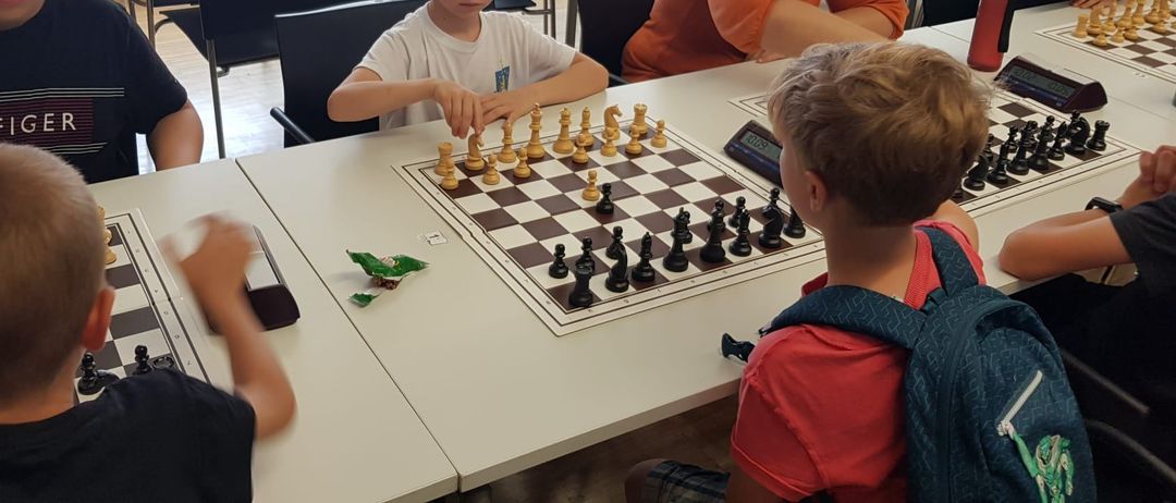 Eine Gruppe von Kindern und Erwachsenen spielt Schach an einem Tisch. Ein Junge konzentriert sich auf sein Spiel.