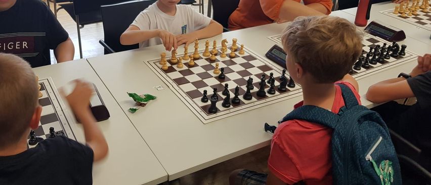 Eine Gruppe von Kindern und Erwachsenen spielt Schach an einem Tisch. Ein Junge konzentriert sich auf sein Spiel.