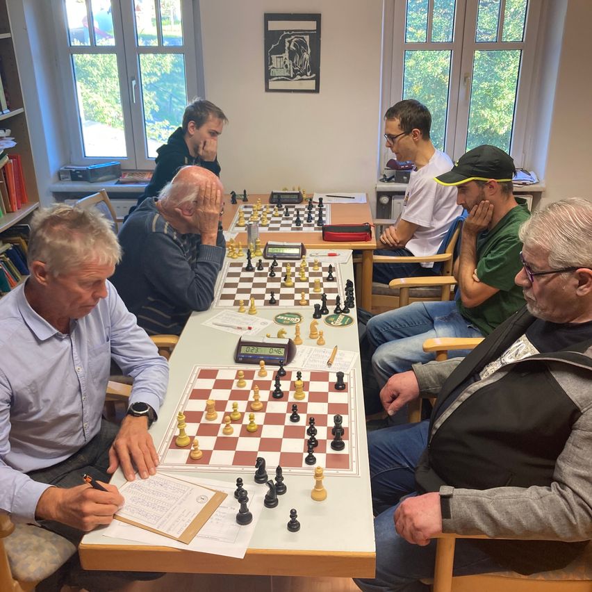 Eine Gruppe von Männern sitzt um einen Tisch herum und spielt Schach.