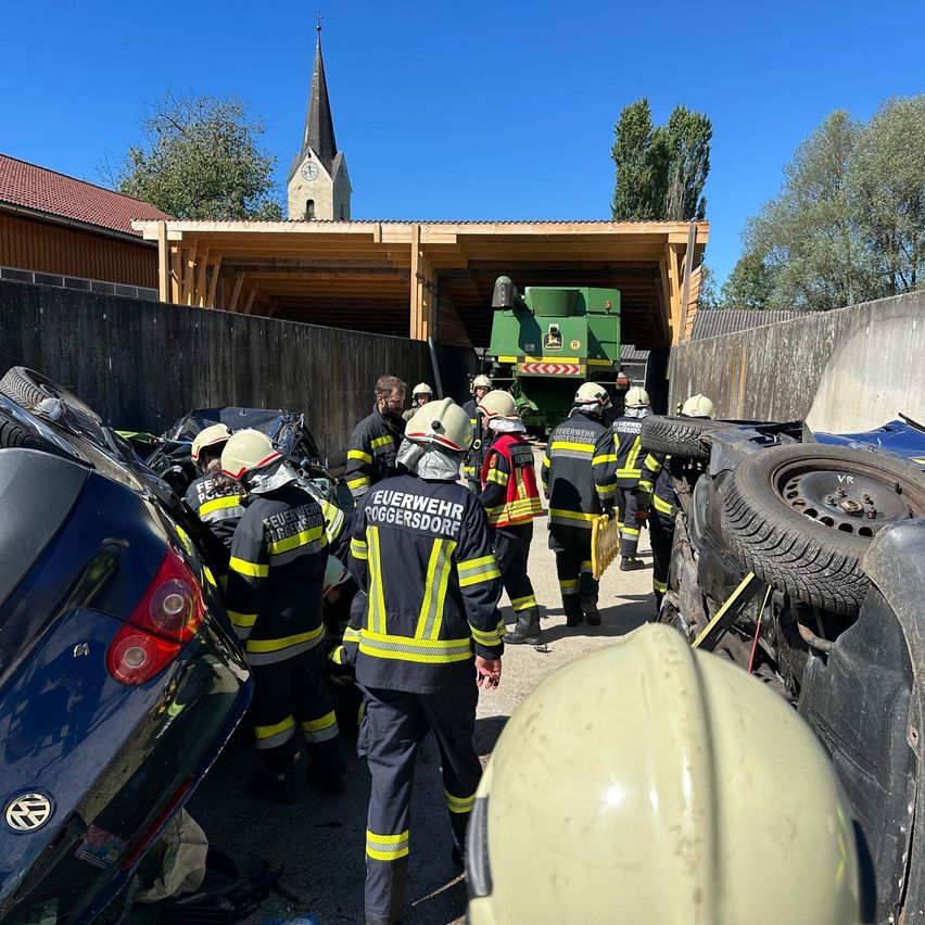 Rettungskräfte stehen um einen Traktor und mehrere beschädigte Autos herum, möglicherweise aufgrund eines Unfalls. Sie tragen Helme und Uniformen mit reflektierenden Streifen.