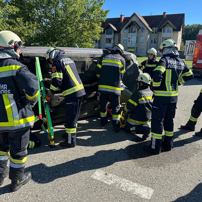 Eine Gruppe von Feuerwehrleuten in Schutzausrüstung arbeitet an einem Fahrzeug im Freien, möglicherweise bei einer Rettungsaktion.