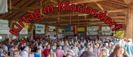 Eine große Menschenmenge versammelt sich drinnen, wahrscheinlich bei einem Festival oder einer Veranstaltung, mit Bannern und Schildern im Hintergrund. Das Datum und die Uhrzeit der Veranstaltung sind prominent angezeigt.