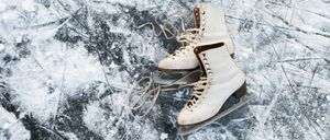 Ein Paar weißer Schlittschuhe mit braunen Schnürsenkeln und Klingen liegt auf einer verschneiten, eisigen Oberfläche.