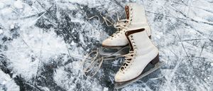 Ein Paar weißer Eislaufschuhe mit braunen Sohlen liegt auf einer verschneiten Oberfläche. Schnee bedeckt den Boden, und die Schlittschuhe sind geschnürt.