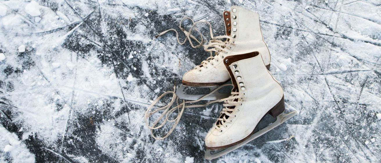 Ein Paar weißer Eislaufschuhe mit braunen Sohlen liegt auf einer verschneiten Oberfläche. Schnee bedeckt den Boden, und die Schlittschuhe sind geschnürt.