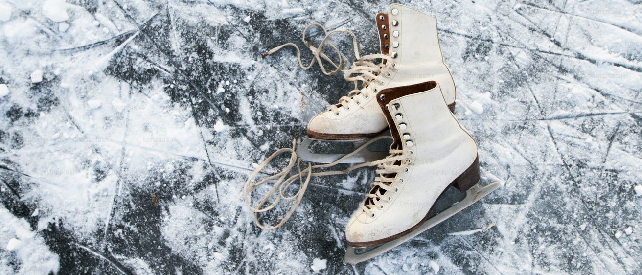 Ein Paar alte Eislaufschuhe mit braunen Kufen und geschnürten Schnürsenkeln liegen auf einer gefrorenen Oberfläche. Das Eis zeigt Abnutzungsspuren mit Kratzern und Schneeflecken.