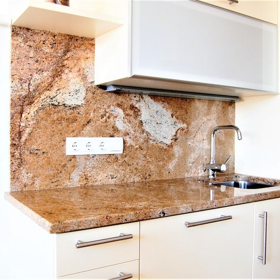 Eine Küche mit Granitarbeitsplatte, einem Waschbecken und einem Wasserhahn. Über dem Waschbecken befindet sich eine Steckdose und die Wand ist mit braunem Granit gefliest.
