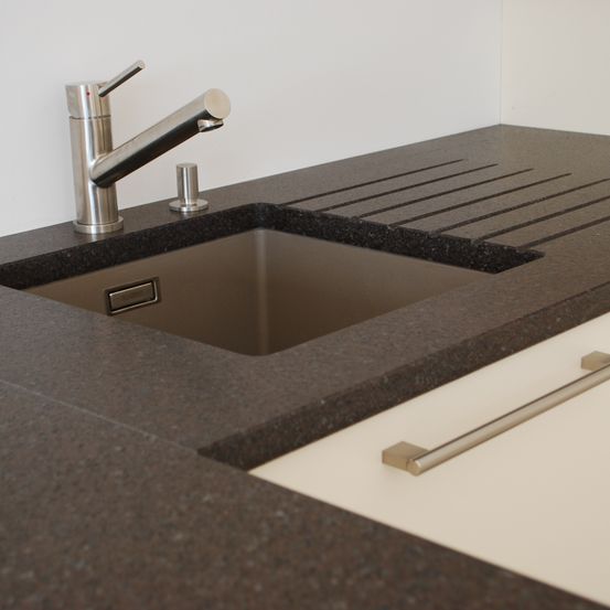 Nahaufnahme eines modernen Küchenspülbeckens mit einem Edelstahlhahn und Abfluss, auf einer schwarzen Granitarbeitsplatte mit einem weißen Schrank darunter.