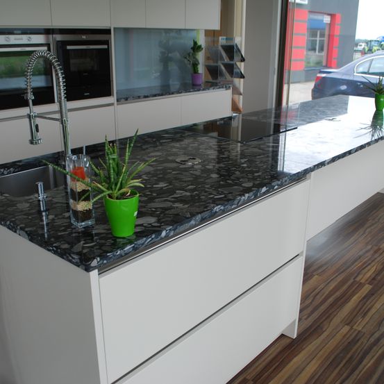 Eine moderne Küche mit weißen Schränken, einer schwarzen Granitarbeitsplatte, einem Waschbecken mit Wasserhahn, einem Topf und einem Herd auf der Arbeitsplatte.