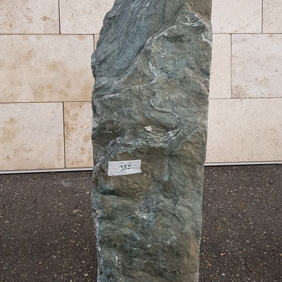 Ein großer grauer Stein steht vor einer beigen gefliesten Wand, mit einem weißen Etikett, das 355 markiert ist.