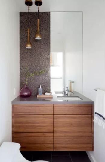 Ein modernes Badezimmer mit Holzschränken, einem großen Spiegel und zwei hängenden Lampen. Das Waschbecken ist mit einem Wasserhahn ausgestattet, und die Arbeitsplatte hat eine Pflanze und eine Flasche.