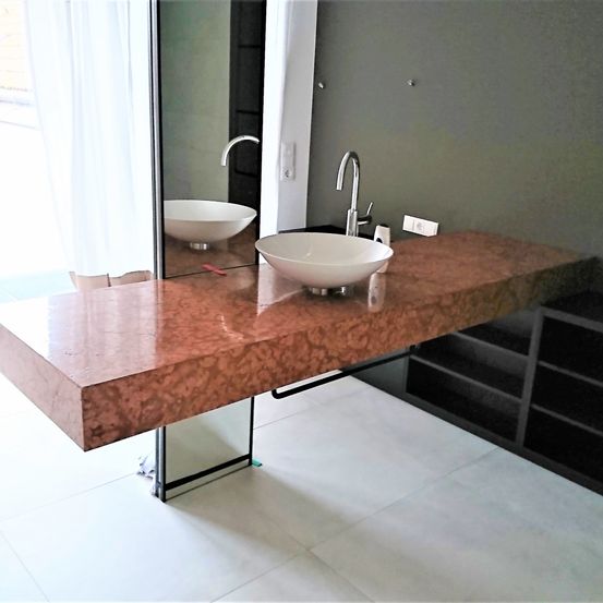 Ein modernes Badezimmer mit einem großen Spiegel, einem Waschbecken und einem Wasserhahn. Der Waschtisch ist aus rosa Marmor und hat ein schlankes Design.