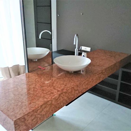 Ein Badezimmer mit einer kupferfarbenen Arbeitsplatte, einem weißen Waschbecken und einem Spiegel mit der Reflexion eines Waschbeckens und eines Wasserhahns.
