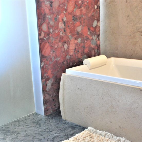 Ein Badezimmer mit einer weißen Badewanne und einer roten Marmorwand. Ein weißer Handtuch liegt auf dem Boden.