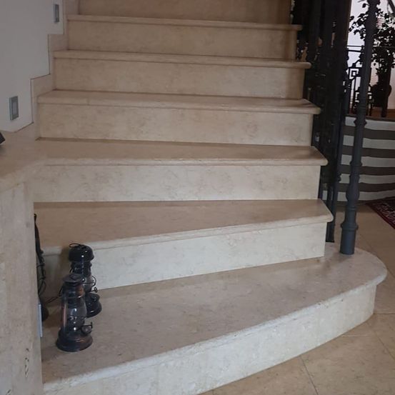 Eine Marmortreppe mit schwarzem Geländer auf der rechten Seite und zwei Laternen auf der linken Seite.