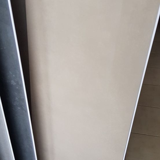 Eine Nahaufnahme eines beigen Panels, wahrscheinlich ein Teil eines Möbelstücks, mit einem weißen Rand rechts und einem dunkelgrauen Rand links.