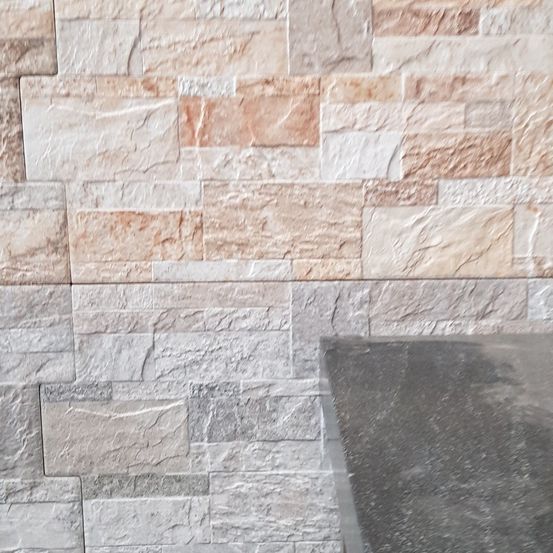 Eine Nahaufnahme einer Steinmauer mit verschiedenen Beige- und Grautönen. Die Wand hat eine strukturierte Oberfläche, die ihr ein rustikales Aussehen verleiht.