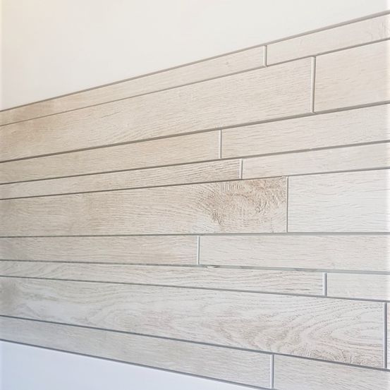 Eine Wand mit strukturiertem Holzmuster, hell in der Farbe, möglicherweise eine Badezimmerwand.