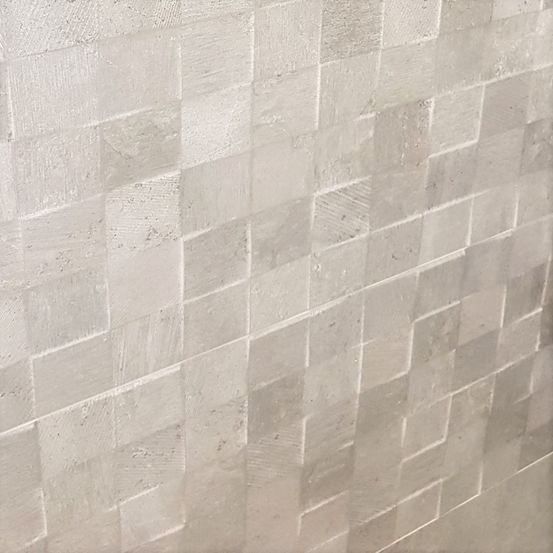 Eine Nahaufnahme einer strukturierten, hellgrauen Wand mit einem Rastermuster, wobei jedes Quadrat leicht in Helligkeit und Textur variiert und ein modernes und minimalistisches Aussehen vermittelt.