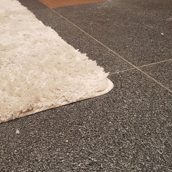 Ein beigefarbener Schlingenteppich liegt auf einem grauen Fliesenboden mit sichtbaren Fugenlinien, der Teppich hat eine dichte Schlinge.