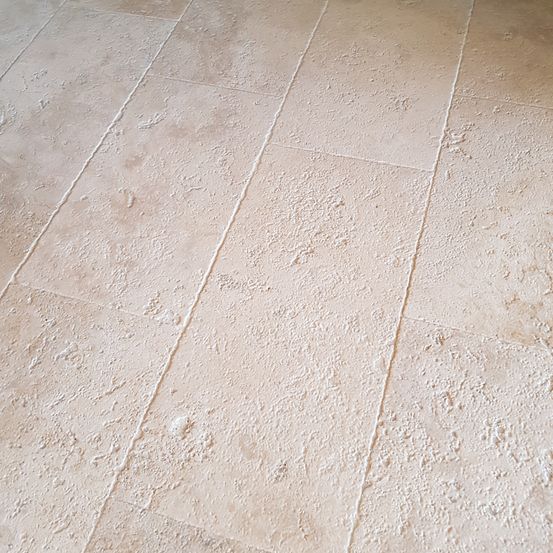 Eine Nahaufnahme eines beigen Fliesenbodens mit sichtbaren Fugenlinien und einer leicht strukturierten Oberfläche.