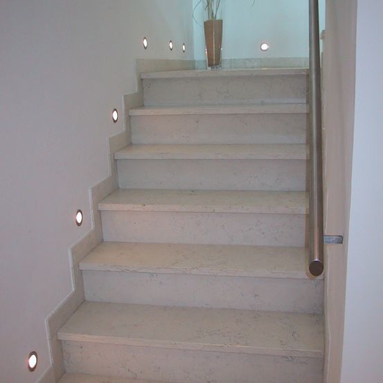 Eine Treppe aus weißem Marmor mit einem Topf auf der obersten Stufe. Die Wände sind weiß und kleine Lichter sind in die Wand eingelassen.