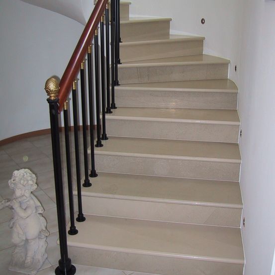 Ein Nahaufnahme einer weißen Treppe mit einem hölzernen Handlauf und schwarzen Metallpfosten. Ein kleiner Statue steht auf dem Boden.