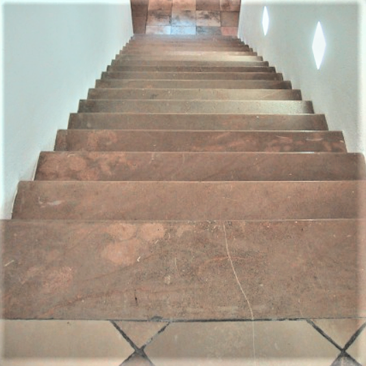 Ein Bild einer Treppe mit braunen Fliesen und weißen Wänden, zwei rautenförmige Lichter sind an der Wand montiert.