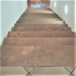 Ein Bild einer Treppe mit braunen Fliesen und weißen Wänden, zwei rautenförmige Lichter sind an der Wand montiert.