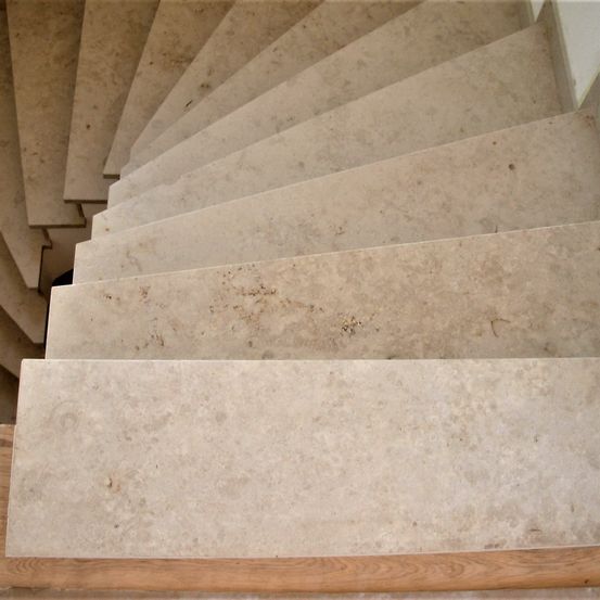 Eine Wendeltreppe mit beigefarbenen Marmorstufen und Holzkanten wird von unten gezeigt. Die Stufen erscheinen sauber mit leichten Unvollkommenheiten.