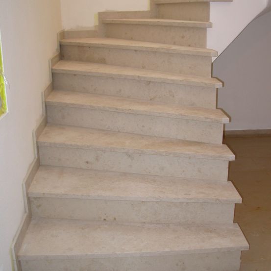 Das Bild zeigt eine Marmortreppe mit geradem Handlauf, die an einer weißen Wand angebracht ist. Die Stufen sind breit und flach und führen nach unten.