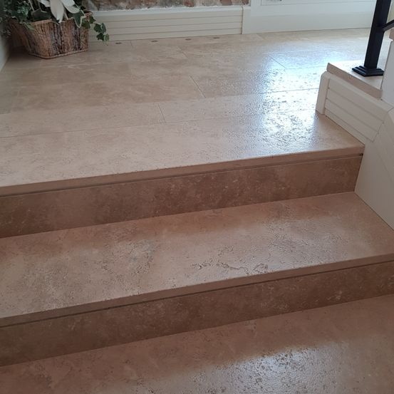 Eine Nahaufnahme einer beigen gefliesten Treppe mit einem Korb mit Pflanzen auf der linken Seite. Die Fliesen haben eine leicht glänzende Textur.