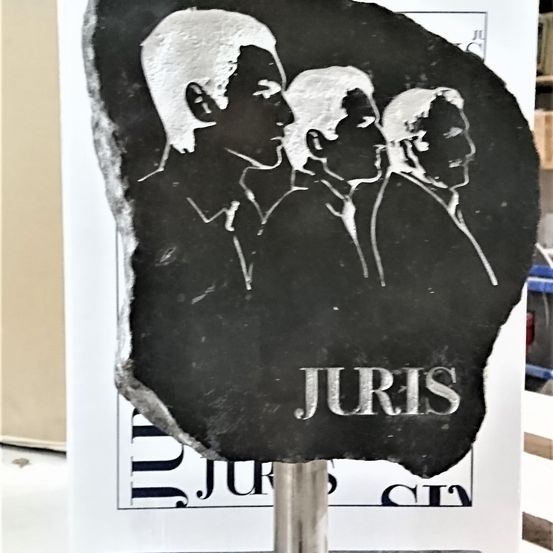 Eine schwarze Steinplatte mit vier Männern in Anzügen, die darauf graviert sind, das Wort 'JURIS' unter den Männern.