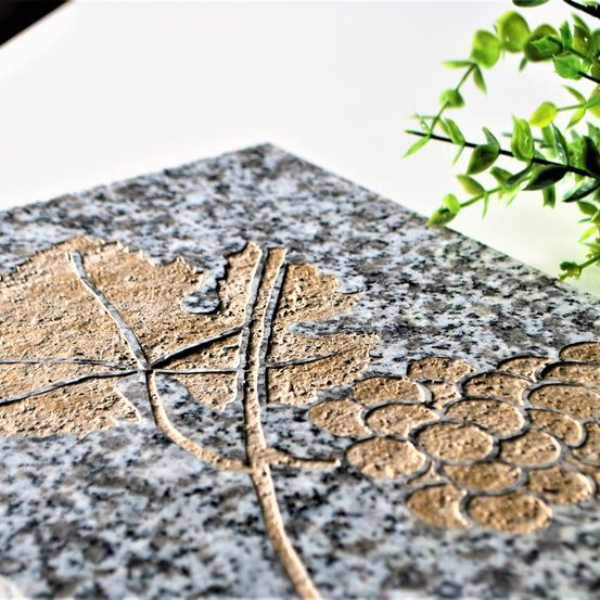Eine Nahaufnahme einer Granitplatte mit einem goldfarbenen Design aus Traubenblättern und Trauben darauf.