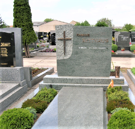 Ein Friedhof mit verschiedenen Grabsteinen. Ein prominenter Grabstein trägt die Aufschrift 'FAMILIE RETHAUS' mit einem Kreuz darauf. Andere Grabsteine und Grünflächen umgeben den Bereich.
