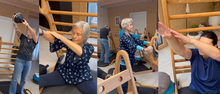 Three people are doing Pilates exercises in a gym. One person is using a weight. Two are seated on exercise benches, one standing.