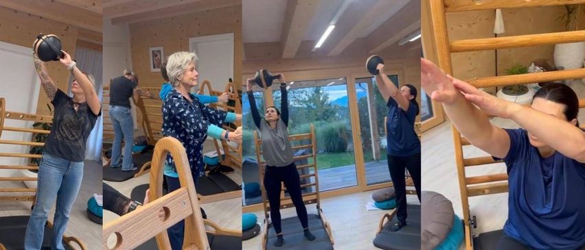 Drei Personen in einem Fitnessstudio, eine ältere Frau und zwei jüngere Frauen. Jede übt mit Gewichten. Die ältere Frau steht und hält Gewichte.