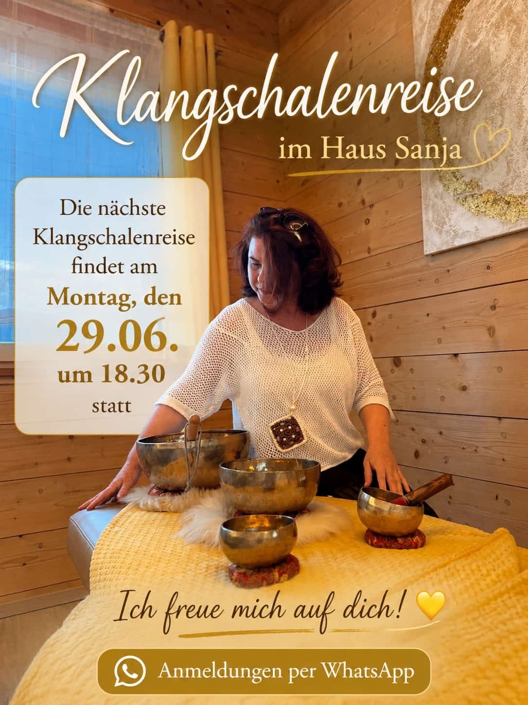 Eine Frau, die einen Holzstab hält, sitzt an einem Tisch mit Schalen, mit einer Holzwand und einem Fenster im Hintergrund. Der Text lautet 'Klangschalenreise im Haus Sanja' und 'Die nächste Klangschalenreise findet am Montag, den 29.06. um 18.30 statt'.