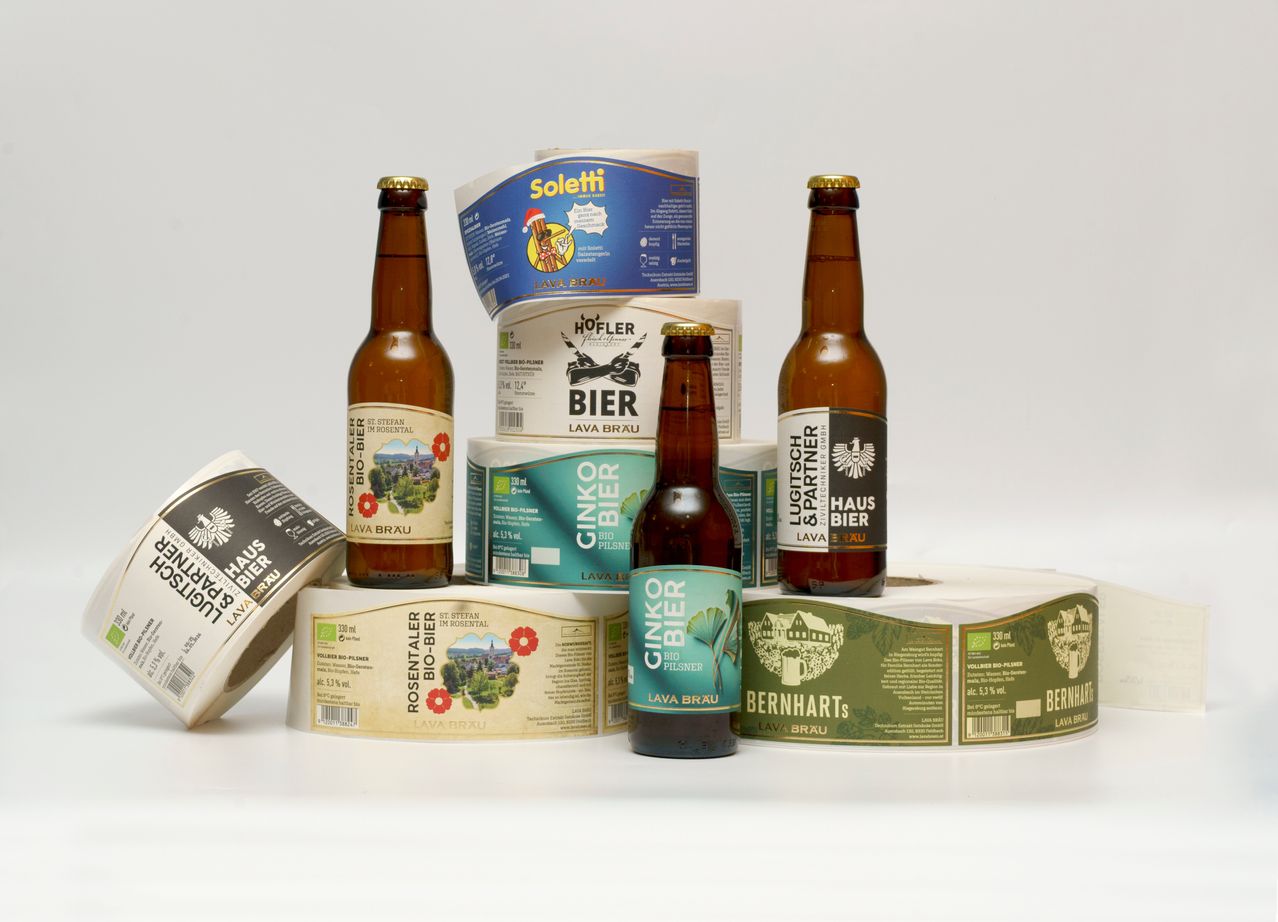 Eine Ausstellung verschiedener Bierflaschen und Etiketten. Mehrere Flaschen haben Etiketten für Marken wie Soletti, Hofler und Lava Brau. Die Etiketten und Flaschen sind auf einem weißen Hintergrund angeordnet.