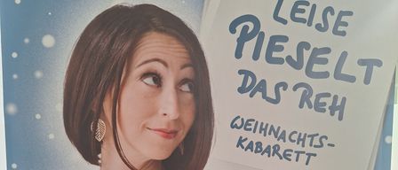 Ein Plakat für ein Weihnachtskabarett mit einer Frau mit kurzen Haaren und einem ernsten Gesichtsausdruck, die ihre Brust mit einer Hand hält. Das Plakat hat einen blauen Hintergrund mit Text und einer Rehen-Illustration.