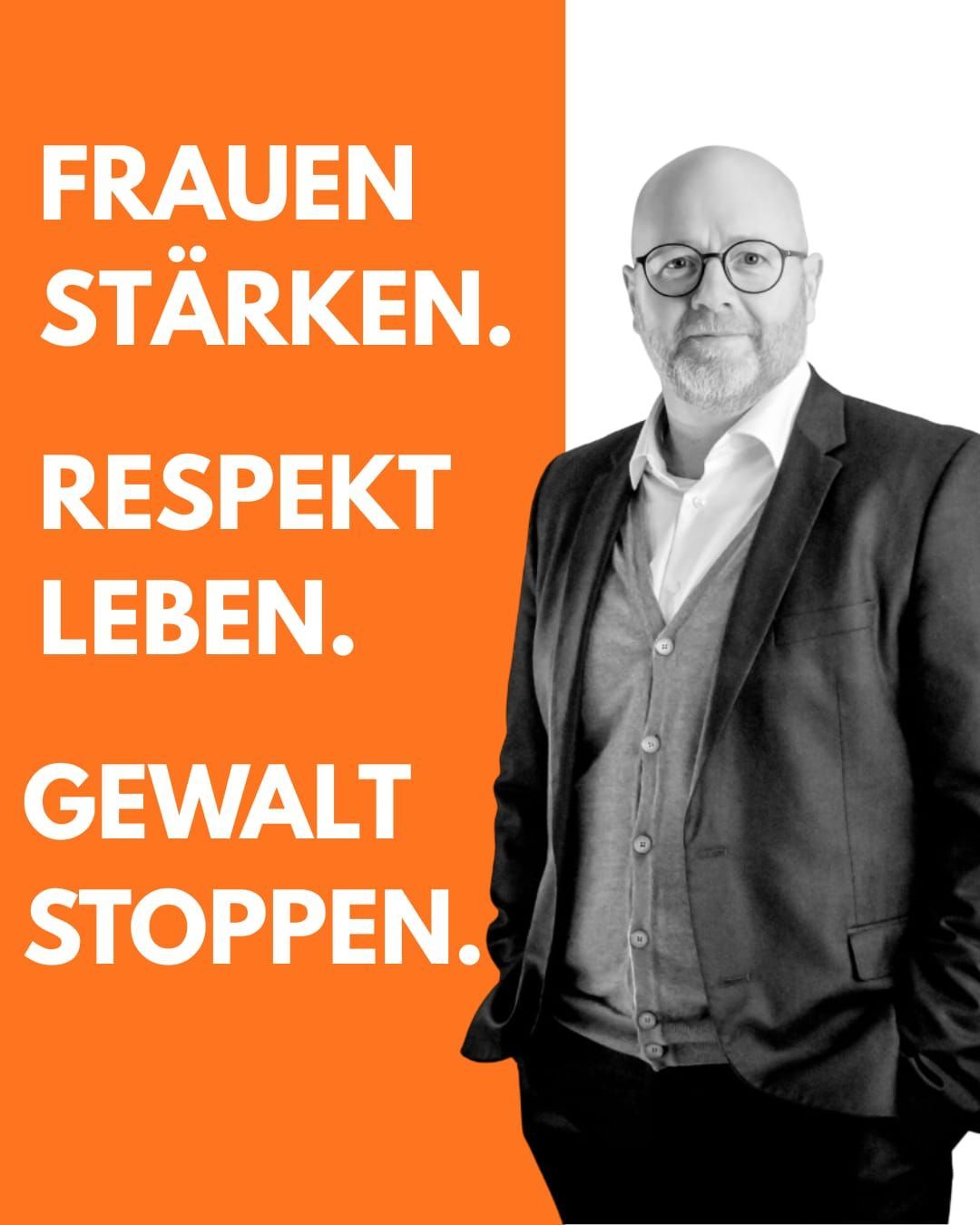 Ein Schwarz-Weiß-Foto eines Mannes, der vor einem orangefarbenen Hintergrund mit deutschem Text 'Frauen stärken, Respekt leben, Gewalt stoppen' steht. Er trägt eine Brille und einen Anzug.