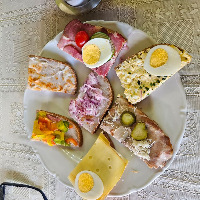Ein Teller mit verschiedenen Sandwiches, darunter Ei, Käse und Fleisch, auf einer Spitzendecke angeordnet.
